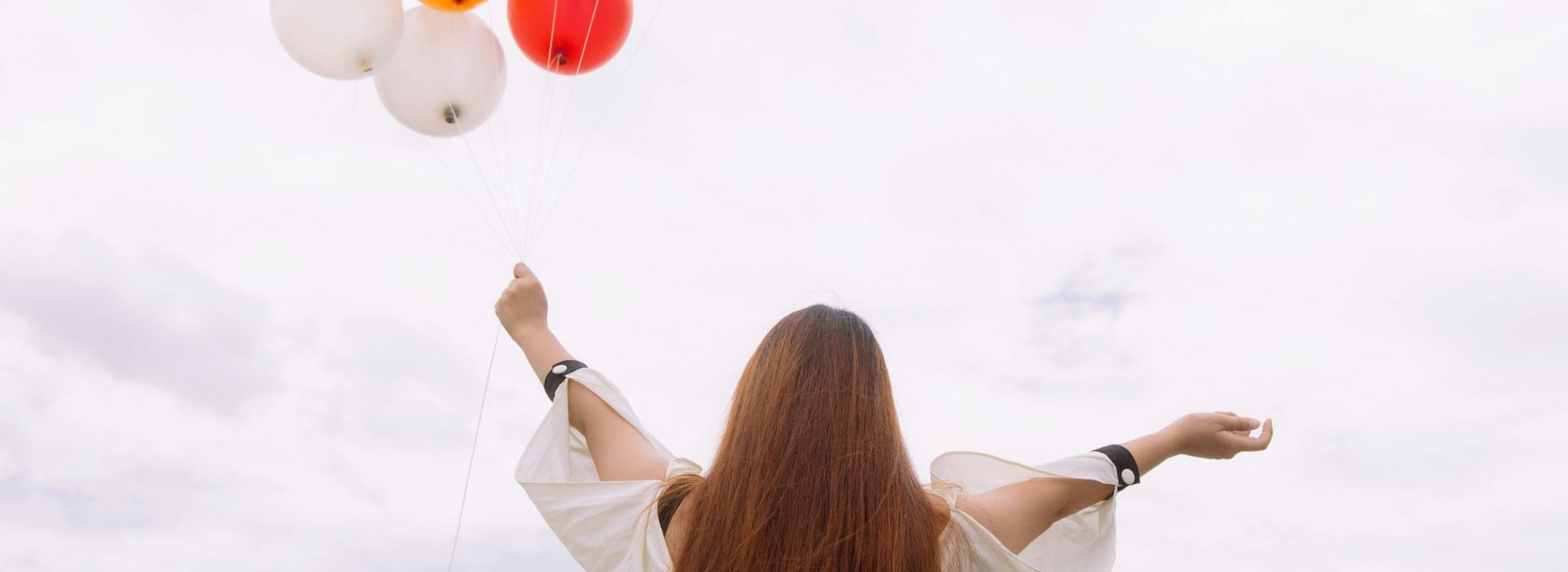 Frau breitet Arme aus und hält Luftballone in linker Hand